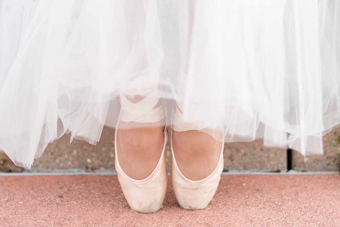 close up of a ballerina's feet while wearing her light pink pointe shoes under a white, tulle skirt